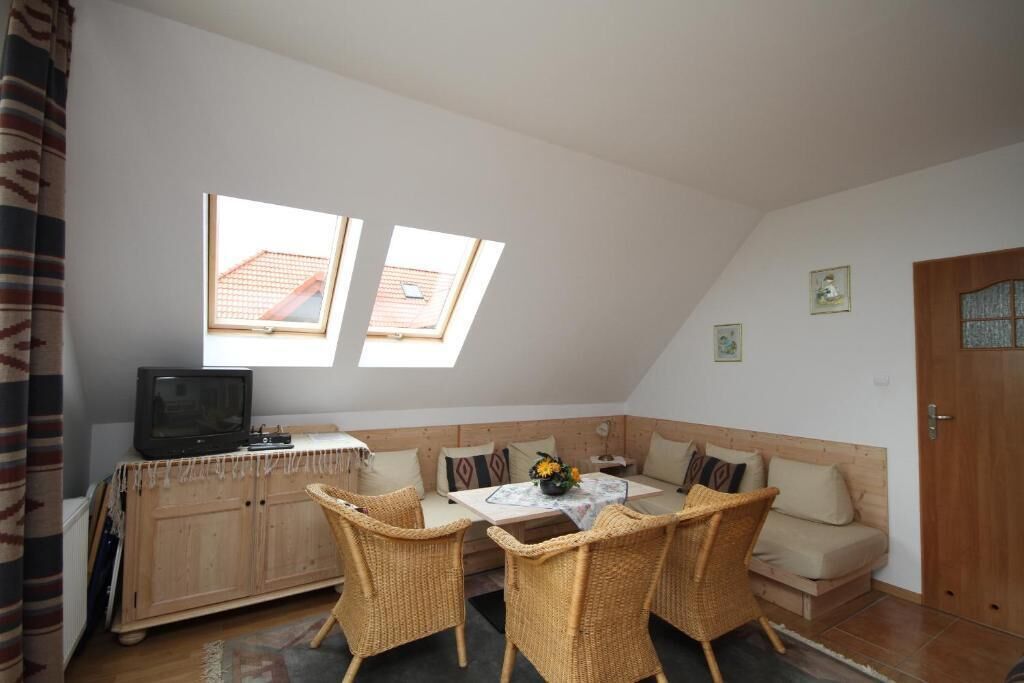Una habitación acogedora con un sofá, una mesa de comedor, sillas de mimbre, un televisor y dos tragaluces.
