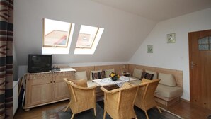 A cozy room with a sofa, a dining table, wicker chairs, a television, and two skylights.