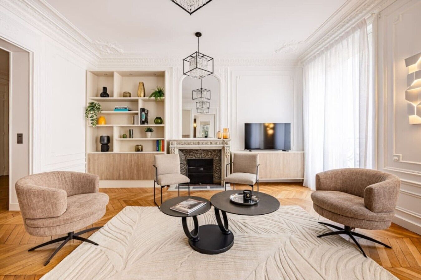 Ein Wohnzimmer mit zwei Sesseln, einem Couchtisch, einem Kamin, einem Fernseher und einem Bücherregal.