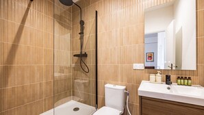 Een moderne badkamer met een douchecabine van glas, een toilet, een wastafel met toiletartikelen en een spiegel boven de wastafel.