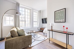 Een moderne woonkamer met een bank, een rond bijzettafeltje, een salontafel en een aan de muur bevestigde televisie.