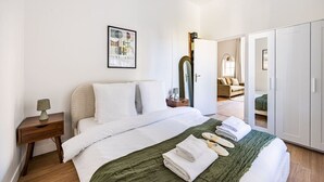 Een slaapkamer met een bed, nachtkastje, spiegel, kledingkast en een deur naar een andere kamer.