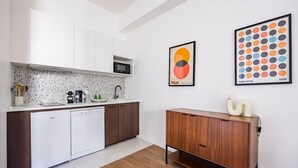 Een moderne keuken met witte kasten, een vaatwasser, een magnetron en een houten servieskast. Er hangen twee ingelijste kunstwerken aan de muur.