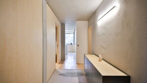 Ein moderner Flur mit minimalistischem Design, ein heller Boden, eine Holztür und eine lange Theke mit einer Vase.