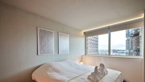 Ein Hotelzimmer mit Bett, Nachttisch, Fenster mit Blick auf Gebäude und zwei Wandbildern.