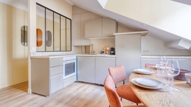 A modern kitchen with white cabinets, a built-in oven, and a dining area with a wooden table and chairs. - 4D. Modern - 2 People - 1 Bedroom - Business - Paris 15 - AC (Paris)
