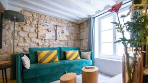 Ein smaragdgrünes Sofa mit gestreiften Kissen, eine Steinsäule, ein Holztisch und eine Vase mit Blumen.