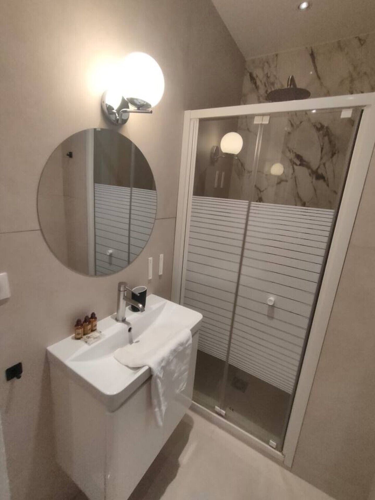 A modern bathroom with a round mirror, a white sink, and a glass-enclosed shower.