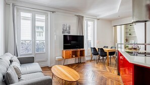 A modern living room with a sofa, TV, dining table, and kitchen area. - Flexible Lease – Paris 2 – Montorgueil – 2-bedroom apartment (Paris)
