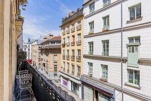 A narrow street with multi-story buildings, balconies, and a storefront with a sign. - Flexible Lease – Paris 2 – Montorgueil – 2-bedroom apartment (Paris)