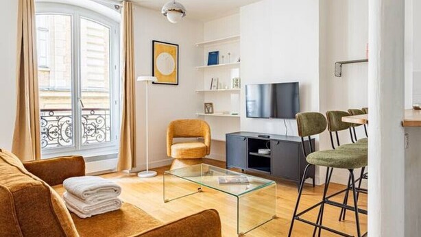 Un salon moderne comprenant un canapé, une table basse en verre, un téléviseur et un coin repas avec des chaises.