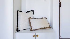 Um banco branco com duas almofadas, um espelho e uma porta com moldura de madeira.