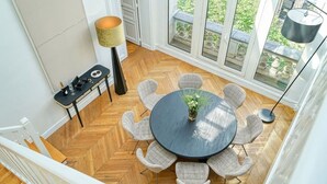 En matplats med ett runt bord, sex stolar, en vas med blommor, ett litet bord med en flaska och glas, och en golvlampa.