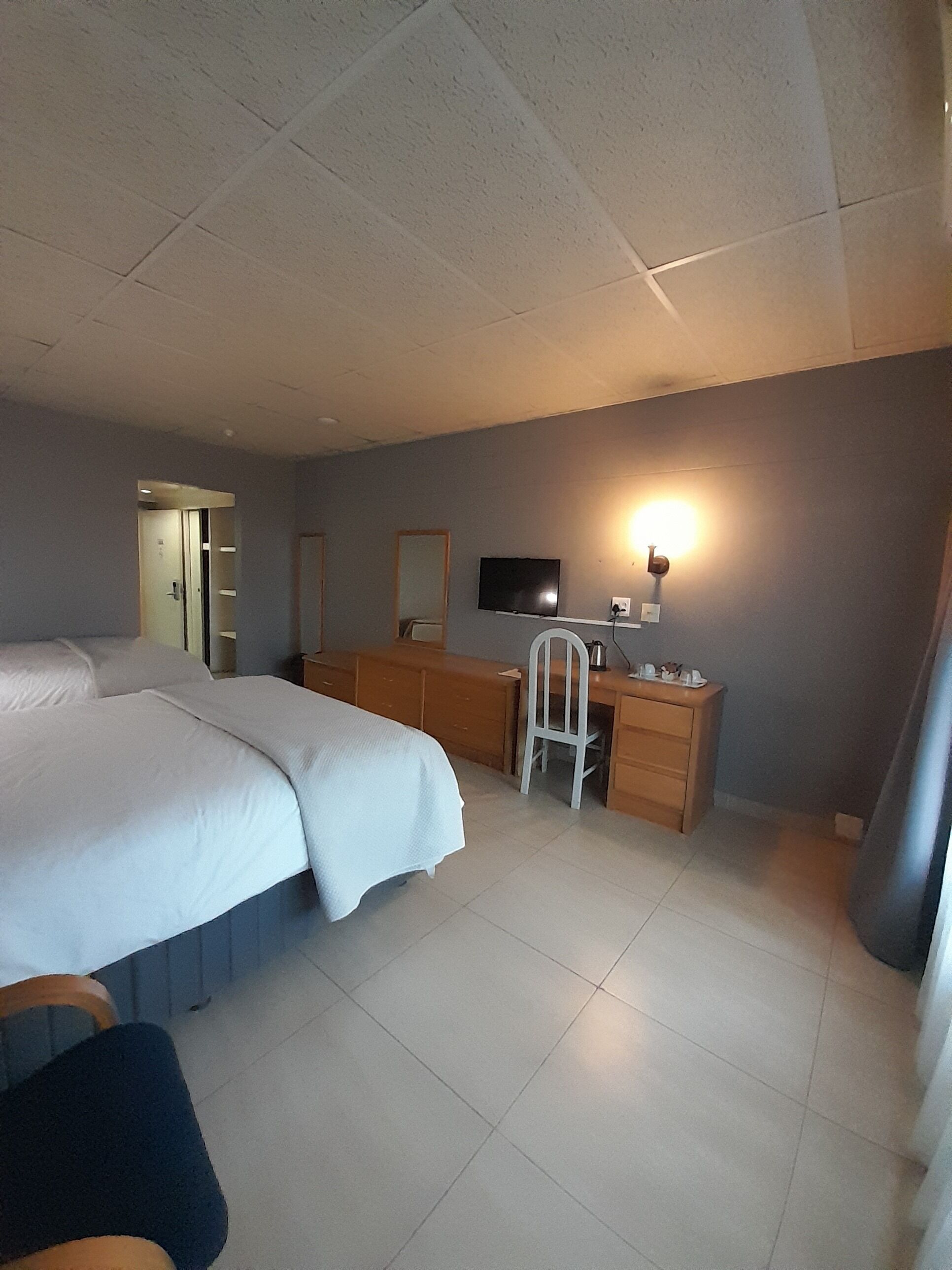 A hotel room with a bed, a desk, a chair, a television, and a mirror.