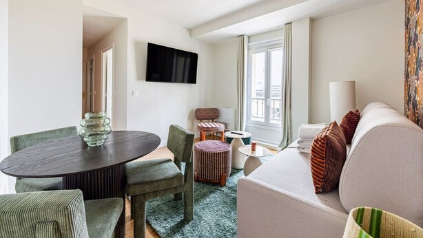 A modern living room with a round dining table, a sofa, a TV mounted on the wall, and a window with curtains. - Modern#ArcDeTriomphe#4people#ChampsÉlysées (Paris)