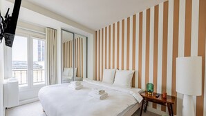 A hotel room with a large bed, a mirror, a bedside table with a lamp, and a view of the outside. - Modern#ArcDeTriomphe#4people#ChampsÉlysées (Paris)