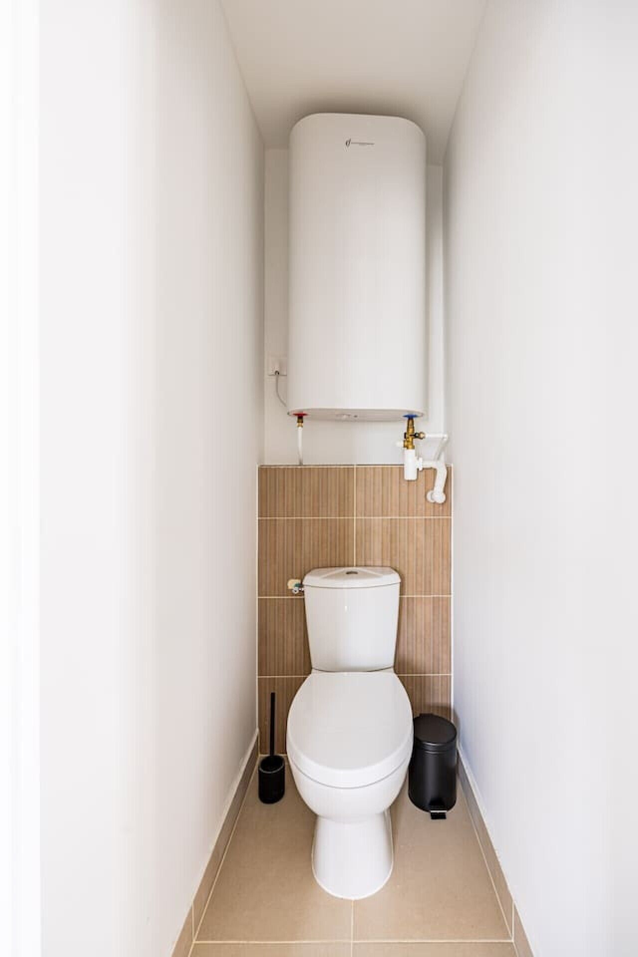 Un bagno piccolo e stretto con il water, un serbatoio bianco e un muro piastrellato.