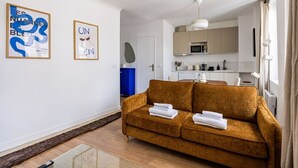 A modern living room with a sofa, a kitchen in the background, and artwork on the walls. - 3. Apartment - 2 people - 1 bedroom - Mouffetard - Sorbonne (Paris)