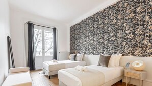 Een slaapkamer met twee bedden, een bankje, een nachtkastje en een grote wand met bloemenprint.