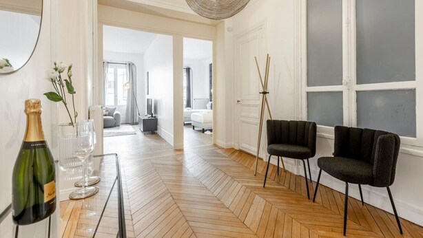 Een ruime kamer met een visgraatvloer, een groot raam en een moderne stoel.
