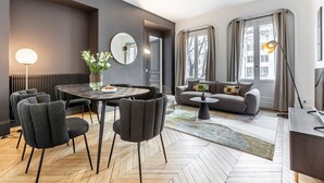 Een moderne woonkamer met een eethoek, een zithoek en een groot raam met gordijnen.