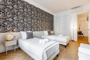 Een moderne hotelkamer met twee bedden, een wand met een groot bloemenmotief, een nachtkastje met een lamp en een houten vloer.