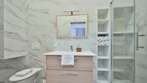 Een moderne badkamer met een marmeren wand, een wastafel met spiegel, toilet, douchecabine en een handdoekrek.