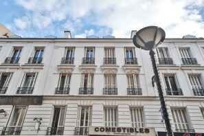 En vit byggnad med många fönster och balkonger, en gatlykta och skyltar med texten ”GRENELLE” och ”COMESTIBLES Charcuterie”.