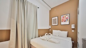 Een slaapkamer met een bed, witte gordijnen, twee kunstwerken in lijsten en een radiator.