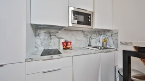 Een compacte keuken met witte kastjes, een ingebouwde magnetron, een spoelbak en een marmeren aanrechtblad.