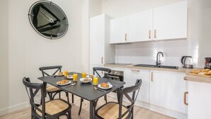 A modern kitchen with white cabinets, a round clock, a dining table with chairs, and breakfast items. - 5. Two bedrooms#Champs-Élysées#Arc de Triomphe#AC (Paris)