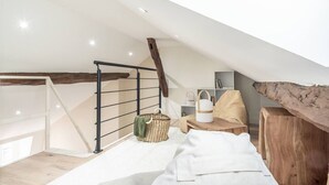 A loft bedroom with a sloped ceiling, a wooden beam, a metal railing, a woven basket, a white chair, and a wooden table. - 5. Two bedrooms#Champs-Élysées#Arc de Triomphe#AC (Paris)