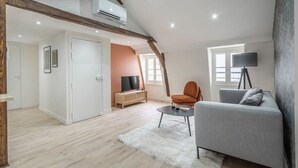 A spacious loft-style room with exposed wooden beams, a flat-screen TV, a grey sofa, and a small table. - 5. Two bedrooms#Champs-Élysées#Arc de Triomphe#AC (Paris)