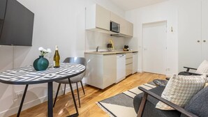 Um espaço compacto com cozinha americana, área de refeições com mesa e cadeiras, e um sofá.