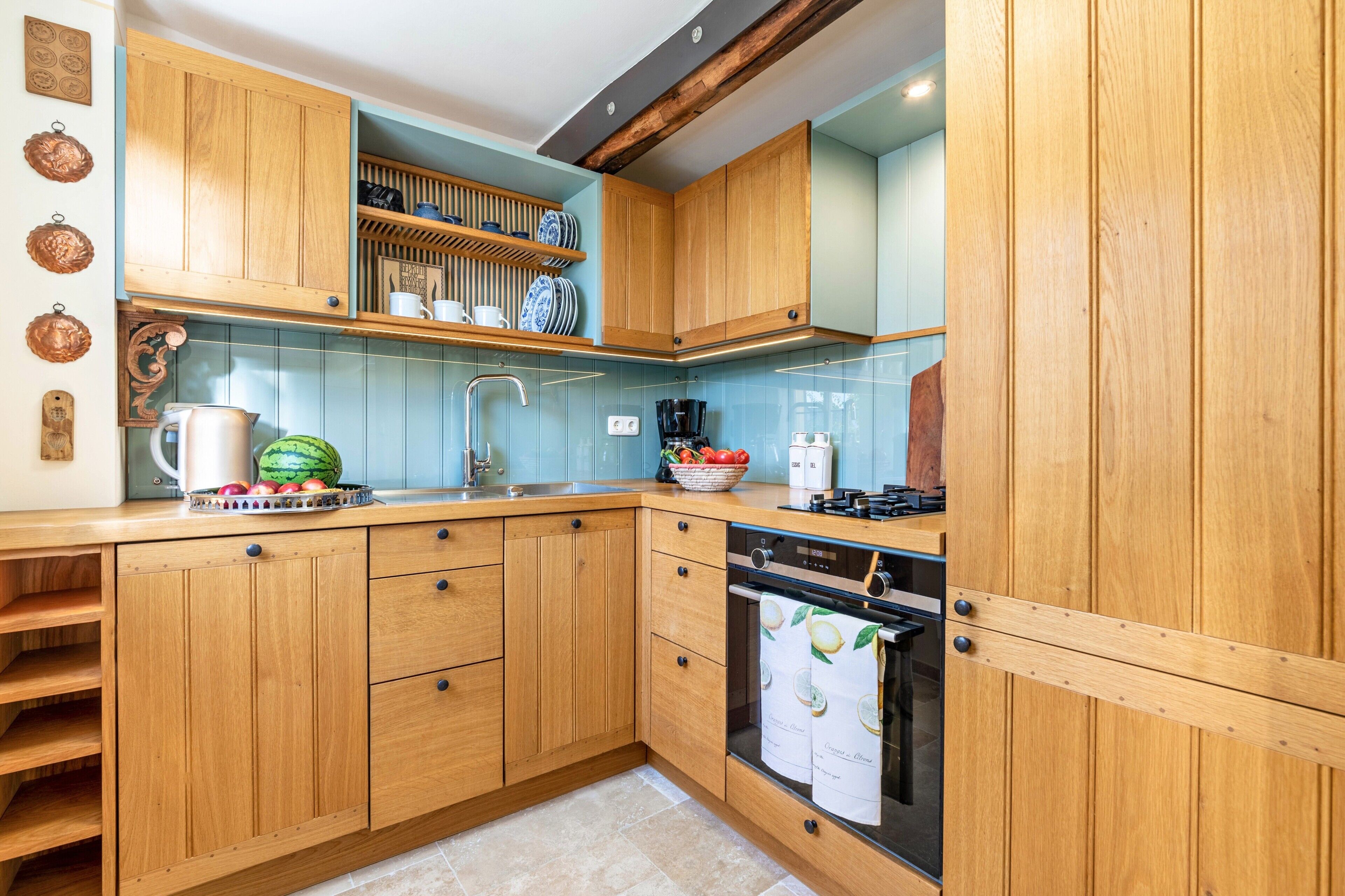 Une cuisine avec des meubles de rangement en bois, un évier, une cuisinière et un plan de travail sur lequel se trouvent divers objets.