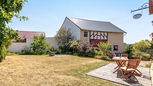 A house with a garden, a wooden deck, and a table with chairs.