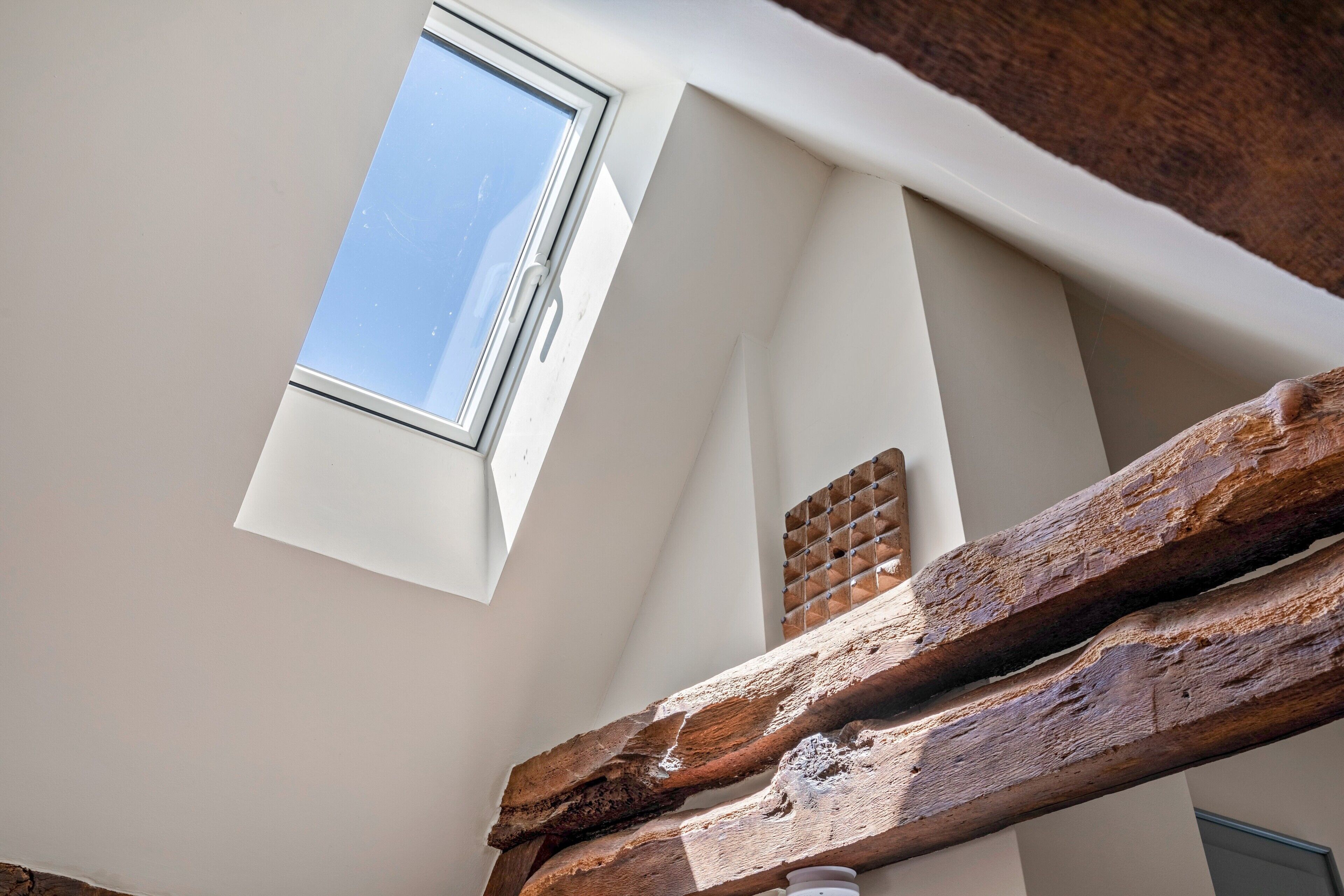 A room with a skylight, a wooden beam, and a brick wall.