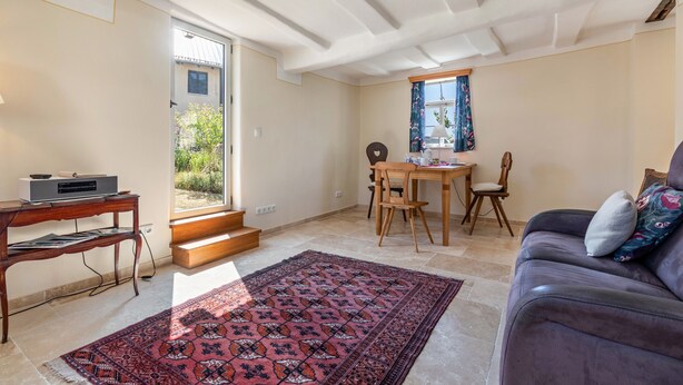 A living room with a sofa, a coffee table, a dining table with chairs, a rug, and a staircase leading to an outdoor area.
