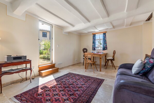 A living room with a sofa, a coffee table, a dining table with chairs, a rug, and a staircase leading to an outdoor area.