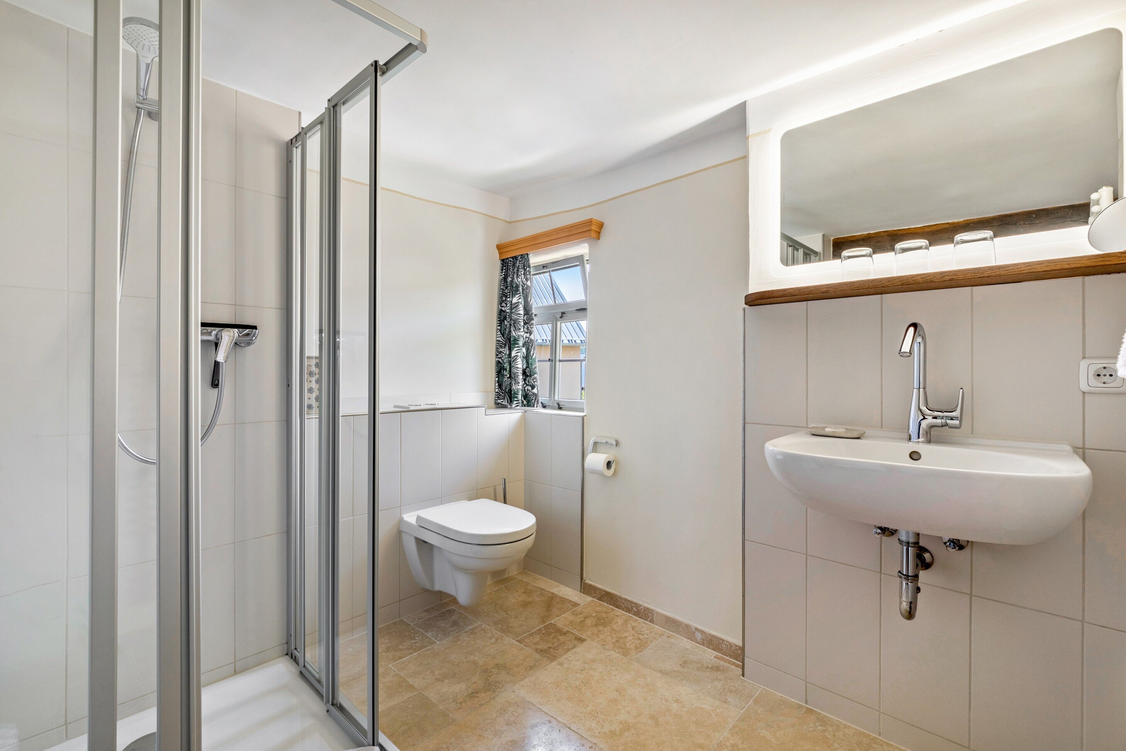 Ein modernes Badezimmer mit Duschkabine aus Glas, Toilette und Waschbecken mit Spiegel darüber.