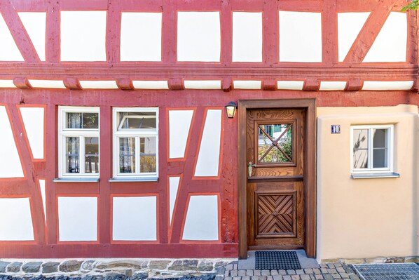A traditional half-timbered building with a wooden door, multiple windows, and a stone foundation.