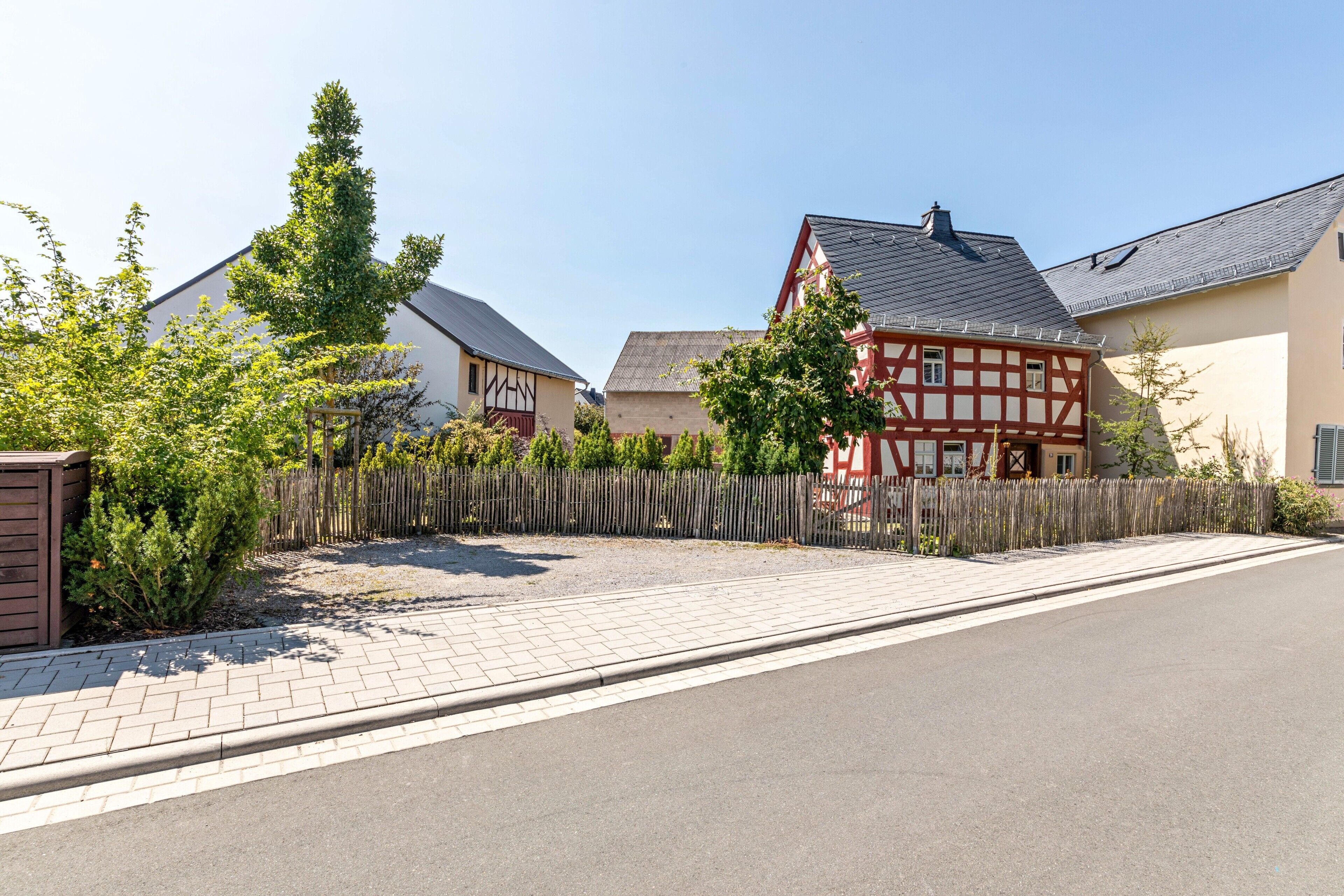 Eine Wohnstraße mit Häusern, einem gepflasterten Bürgersteig und einem Holzzaun.