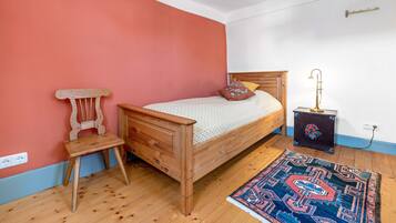 Ein Schlafzimmer mit einem hölzernen Bett, einem Nachttisch, einem Sessel, einem Teppich und einer Steckdose.
