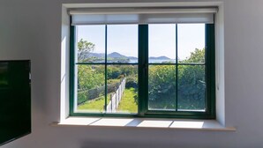 Ein Zimmer mit großem Fenster und Blick auf einen Weinberg sowie entfernte Berge.