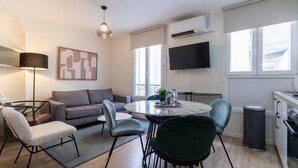 Un salon moderne comprenant un canapé, des fauteuils, une table à manger, un téléviseur et un appareil de climatisation.