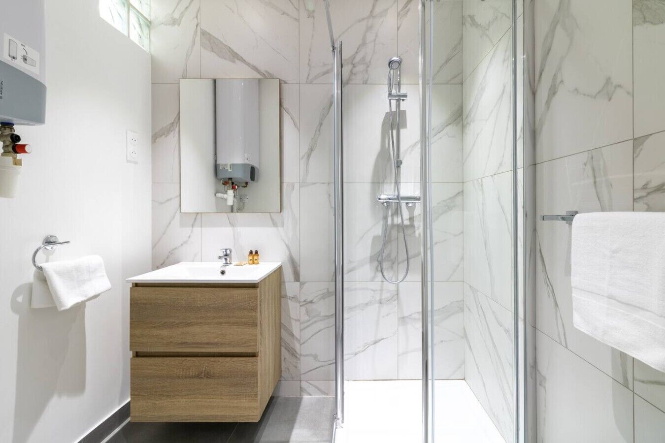 Une salle de bain moderne avec une douche à parois de verre, un meuble-lavabo en bois, un lavabo blanc et un mur recouvert de carreaux de marbre.