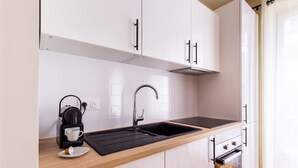 Et moderne køkken med hvide skabe, en sort bordplade, kaffemaskine og vask.