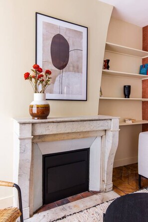 Ein Wohnzimmer mit Kamin, darüber ein gerahmtes Kunstwerk und auf der Kaminbank eine Vase mit Blumen.