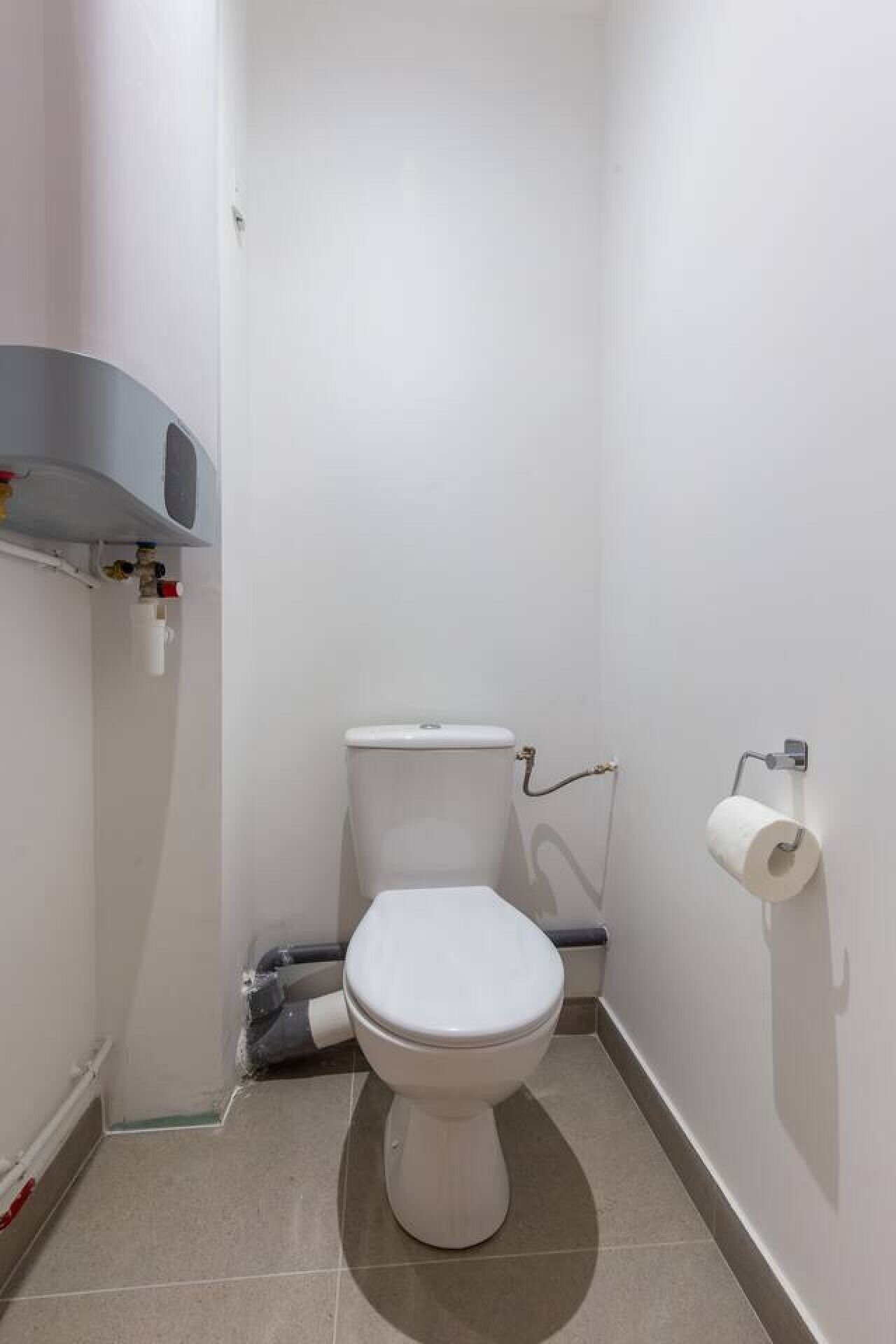 Ein kleines, modernes Badezimmer mit Toilette, Toilettenpapierhalter und einer Duschsteuerung.