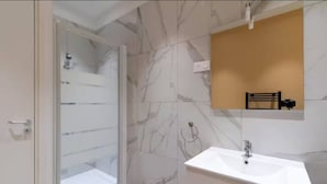 Een badkamer met een douchecabine van glas, een witte wastafel en een houten opbergmeubel.